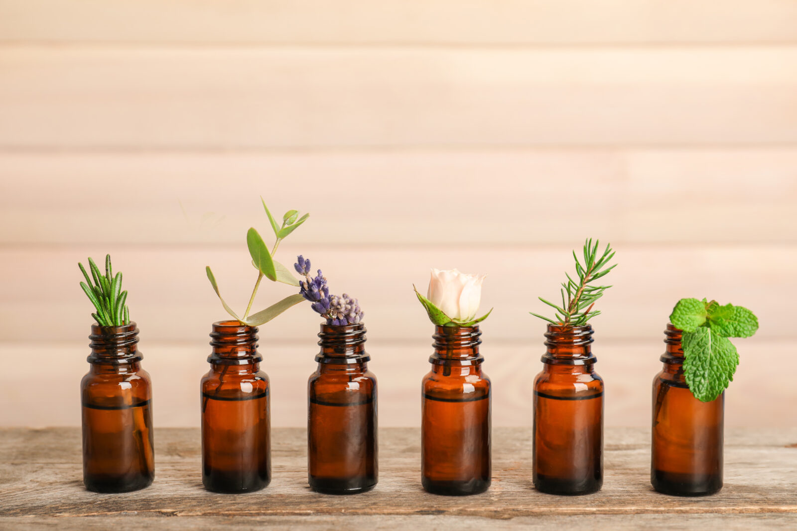 Glass bottles with different essential oils and herbs on wooden background