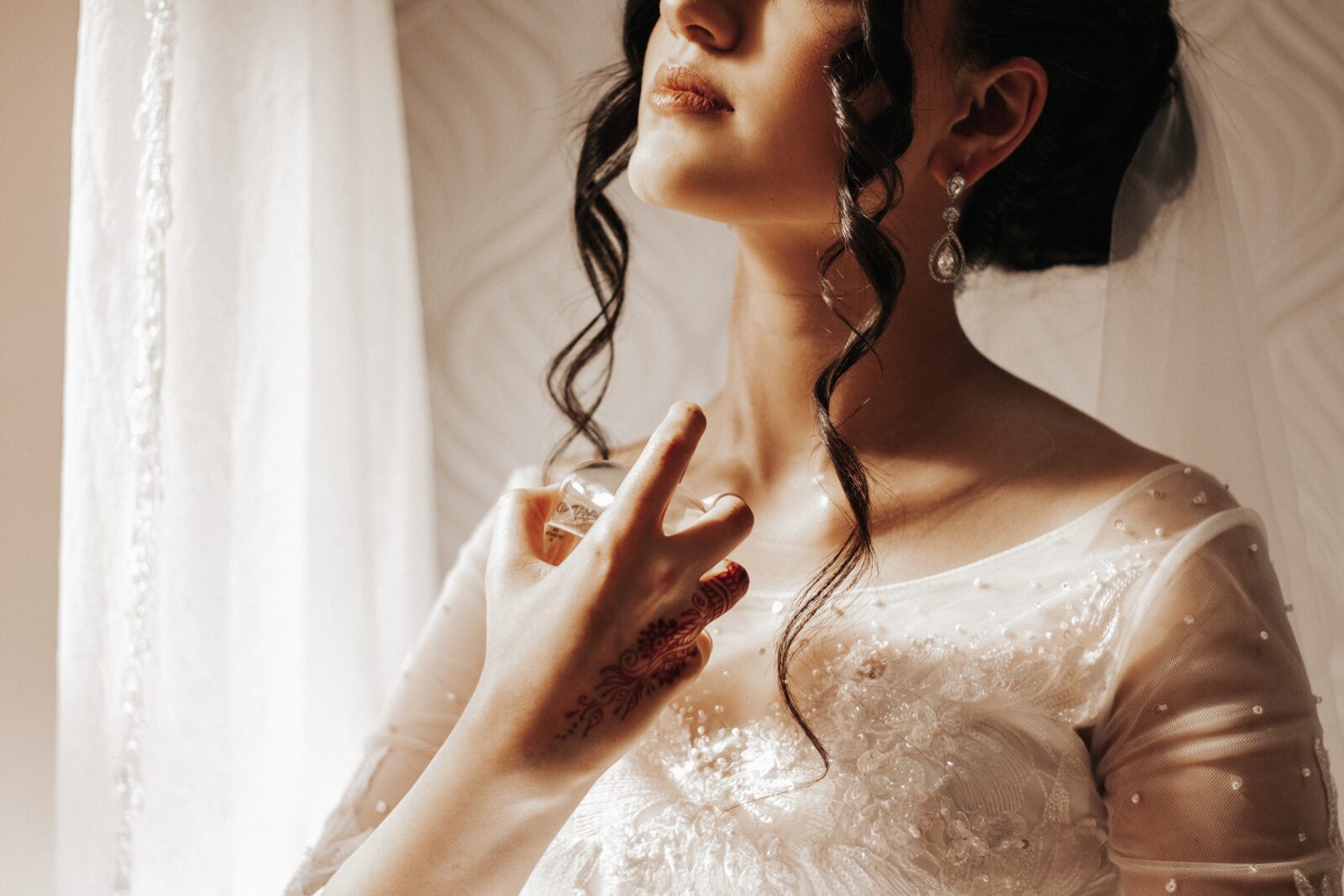 Lady in wedding dress spraying perfume onto neck