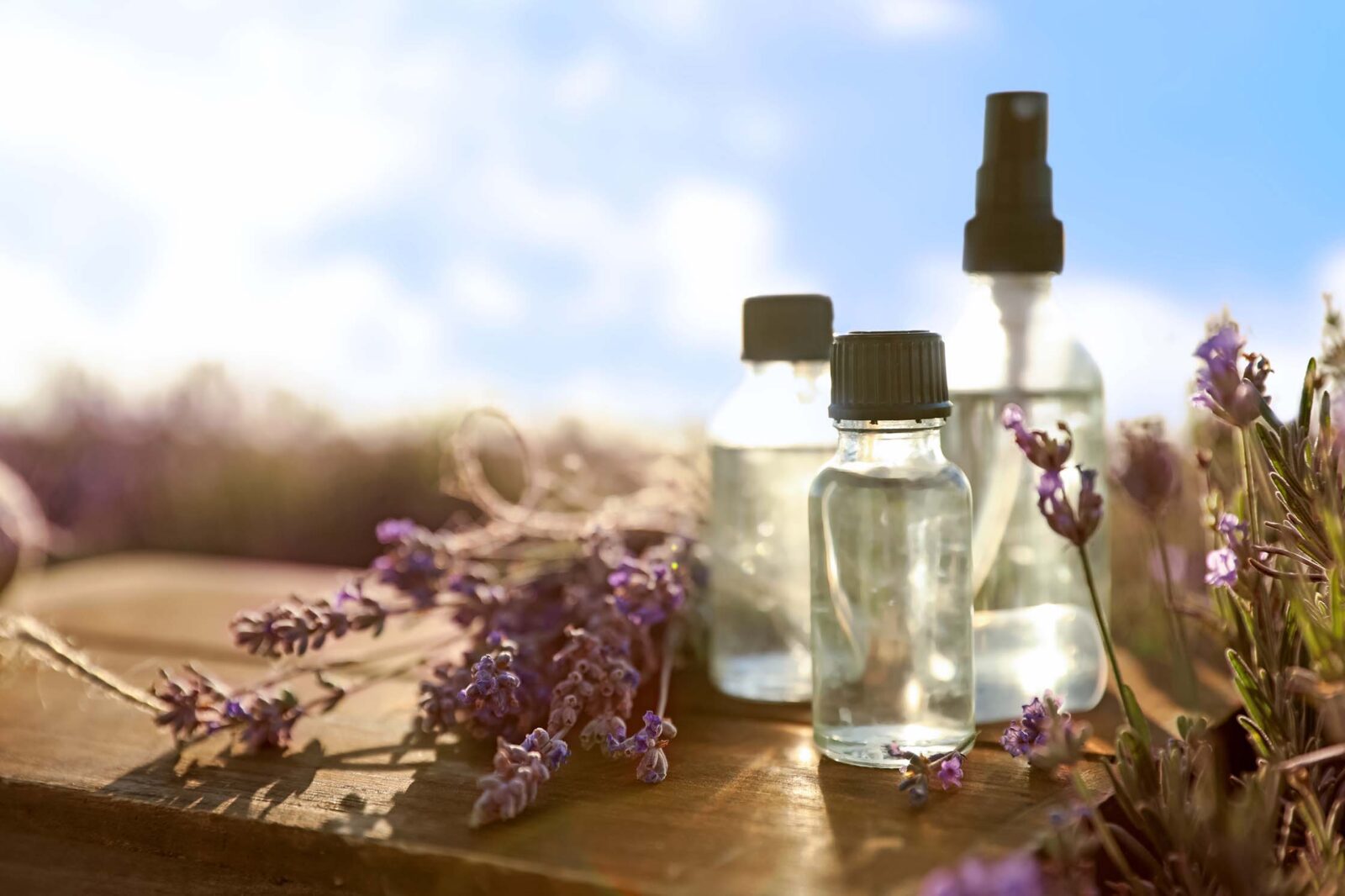 Bottles of lavender essential oil on wooden table in field.